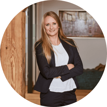 Junge Frau mit langen blonden Haaren und dunklem Blazer in einem Büroflur