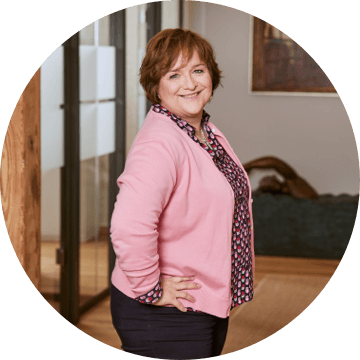 Frau mit kurzem, braunem Haar im rosa Cardigan steht seitlich in einem modernen Büroflur