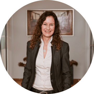 Frau mit lockigem braunem Haar im weißen Hemd und Blazer in einem Büroflur