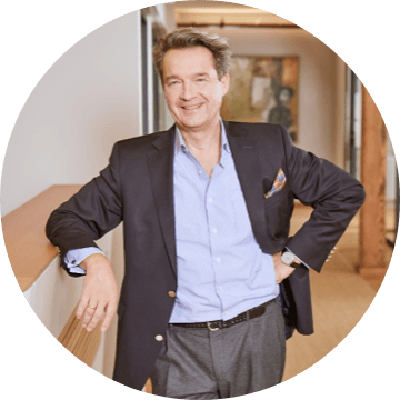 Mann im offenen Hemd und dunklem Sakko lehnt entspannt an einem Tresen im Büro