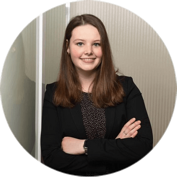 Junge Frau mit langen, glatten Haaren und schwarzem Blazer steht mit verschränkten Armen