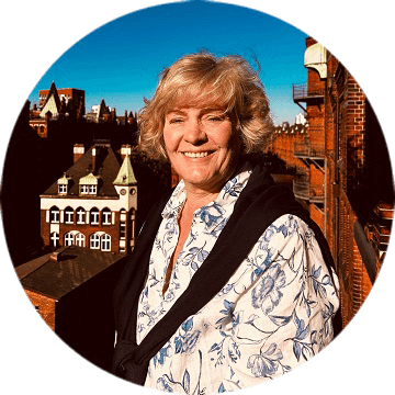 Frau mit blonden Locken in heller Bluse steht auf Balkon mit Speicherstadt im Sonnenlich