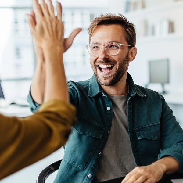 Mann mit Brille und Bart gibt einer weiteren Person ein High-Five im Büro